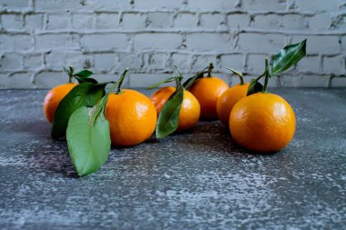 Gray concrete background with a brick wall, tangerines with leaves and twigs view from the top. New Year, in the style of health.