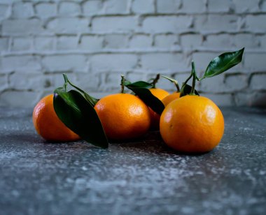 Gray concrete background with a brick wall, tangerines with leaves and twigs view from the top. New Year, in the style of health.