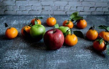 Tuğla duvarlı gri beton arka plan, yapraklı ve dallı mandallar, üstten kırmızı ve yeşil elma manzaralı. Yeni yıl, sağlık tarzında..