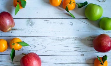 Açık gri ahşap arka plan, yapraklı ve dallı portakallar, üstten kırmızı ve yeşil elma manzarası. Sağlık ve düzgün beslenme biçimi.