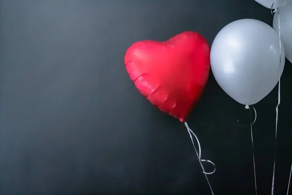 Red heart-shaped balloon and white round air balloon on a black background. valentines day, love. — Zdjęcie stockowe