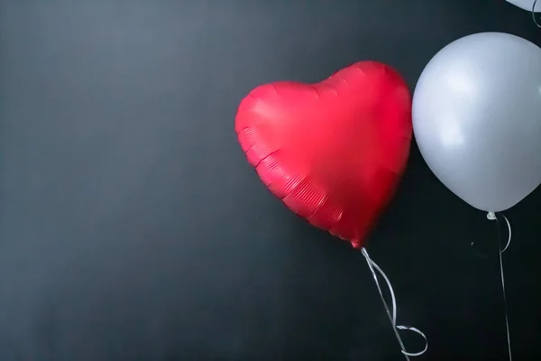 Red heart-shaped balloon and white round air balloon on a black background. valentines day, love. — Zdjęcie stockowe