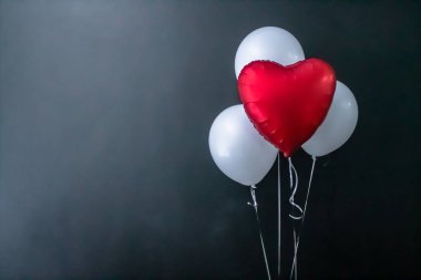 Kırmızı kalp şeklinde balon ve siyah zemin üzerinde beyaz yuvarlak hava balonları. Sevgililer Günü, tatil, aşk.