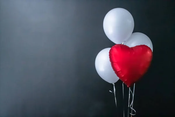 Red heart-shaped balloon and white round air balloons on a black background. Valentines Day, holiday, love.