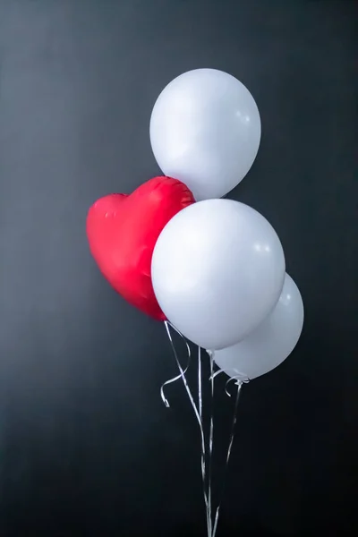 Red heart-shaped balloon and white round air balloons on a black background. Valentines Day, holiday, love. Place for text,