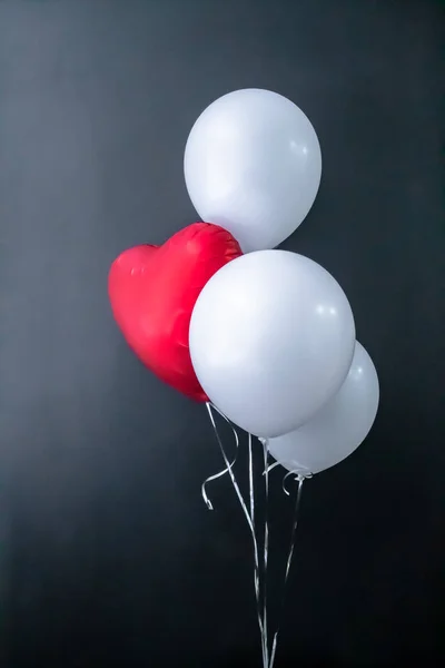 Czerwony balon w kształcie serca i białe okrągłe balony na czarnym tle. Walentynki, wakacje, miłość. Miejsce na tekst, — Zdjęcie stockowe