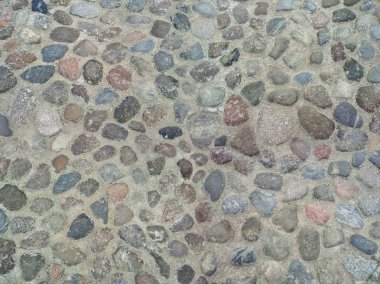 Ancient pavement made of natural stone with rounded cobblestones of various colors and shapes. Texture compiled from several files. Top view.