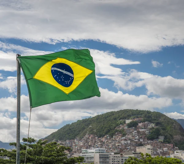 Bandeira brasileira acenando com uma favela ao fundo — Fotografia de Stock