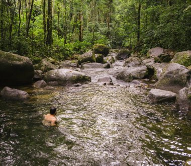 Unidentifiable young male swimming at tropical stream in Penedo, clipart
