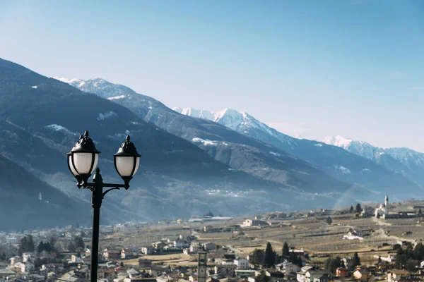 Foco seletivo do poste de iluminação tradicional e mesa de jantar com vista para Sondrio, uma cidade italiana e comuna localizada no coração da região de Valtellina produtora de vinho — Fotografia de Stock