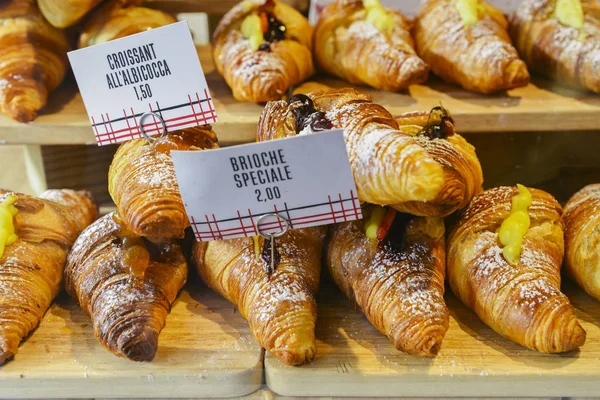 Varios sabores de croissant o como en Italia su llamado brioche en exhibición en una panadería en Milán, Italia con un precio y signo - Albicocca significa mermelada en italiano — Foto de Stock