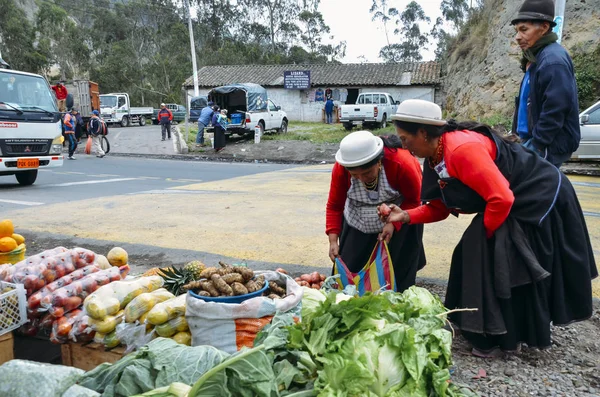 Традиционно одетые эквадорки осматривают овощи на рынке — стоковое фото