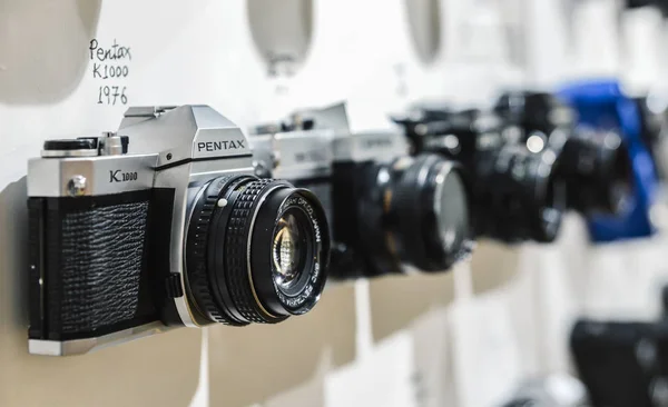 Közelkép a vintage film fényképezőgép Pentax K1000 homályos háttérrel más vintage kamerák a falon látható időszakban 1976-tól — Stock Fotó