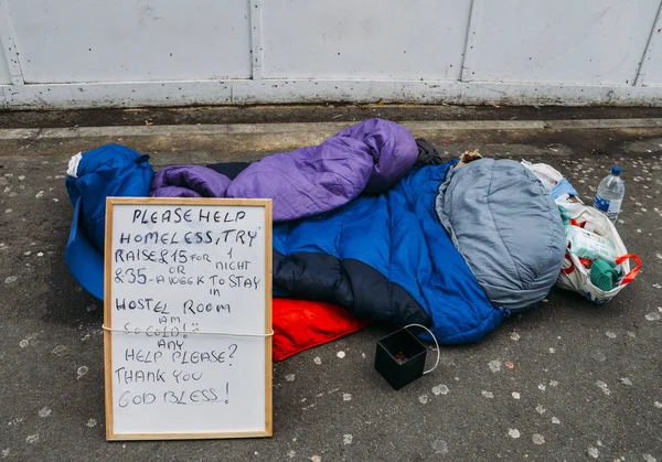 Assine ao lado da calçada de sem-teto com saco de dormir, comida e xícara para a mudança - conceito de austeridade, capturado em Londres, Reino Unido — Fotografia de Stock