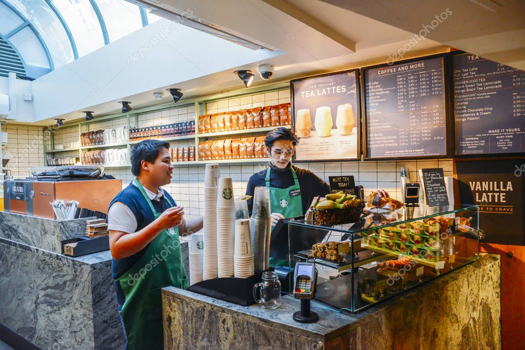 London, UK - March 8, 2018: Two Southeast Asian baristas at a Starbucks coffee house in High Street Kensington, London, UK with some natural light from skylight