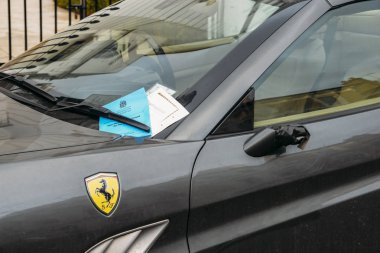 Parking ticket for a a penalty or fine stuck on a luxurious Ferrari cars windscreen, captured in the Royal Borough of Kensington and Chelsea clipart
