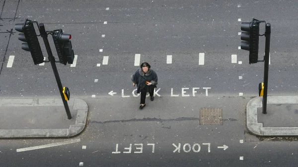 Vista de alta perspectiva de la mujer soltera en la City de Londres cruzando la calle. Icónico mirar a la izquierda y mirar a la derecha signos pintados para ayudar a los turistas de la dirección del tráfico — Foto de Stock