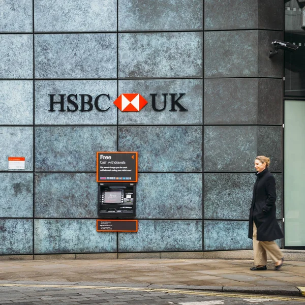 Middle aged woman walks past an Automatic Teller Machine from the HSBC bank advertising free cash withdrawals — Stock Photo, Image