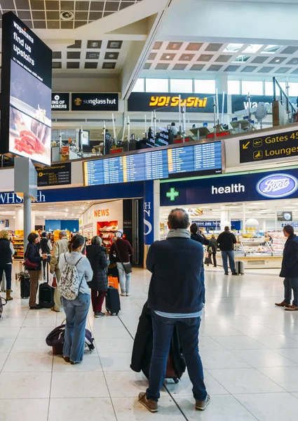 Passengers check their flight information on a digital display at London Gatwick's North Terminal. Various options to shop and eat while passengers wait — Stock Photo, Image