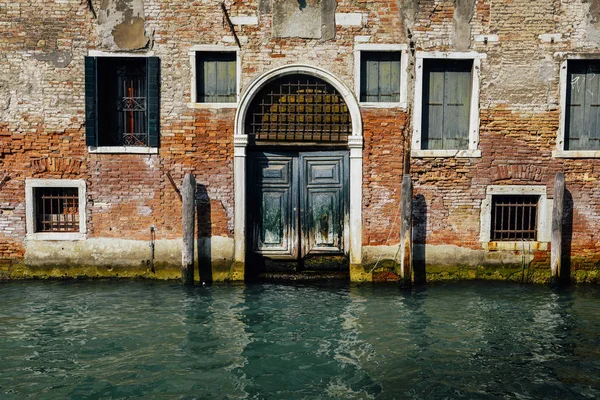 Facade of partially mossy old brick house with wooden vintage door on narrow canal in Venice, Italy. — Stock Photo, Image