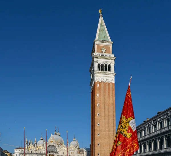 สิงโตปีกแห่งเซนต์มาร์ค ธงเวนิสที่สแควร์ซานมาร์โกในเวนิสกับหอคอยแคมปานิลซานมาร์โก . — ภาพถ่ายสต็อก