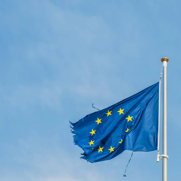 European Union flag on a mast proudly moving in the wind despite the ripped up pieces of cloth on the edges which is perhaps a metaphor for the serious crisis currently facing the economic block. — Stock Photo, Image