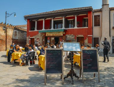 Turistler küçük bir kafe terasta güneşli bir günde Murano Adası'nda oturuyorlar