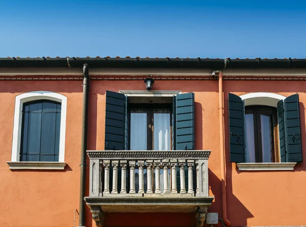 Πορτοκαλί τοίχο του σπιτιού με ένα παράθυρο με τα μπλε παραθυρόφυλλα και μπαλκόνι. — Φωτογραφία Αρχείου