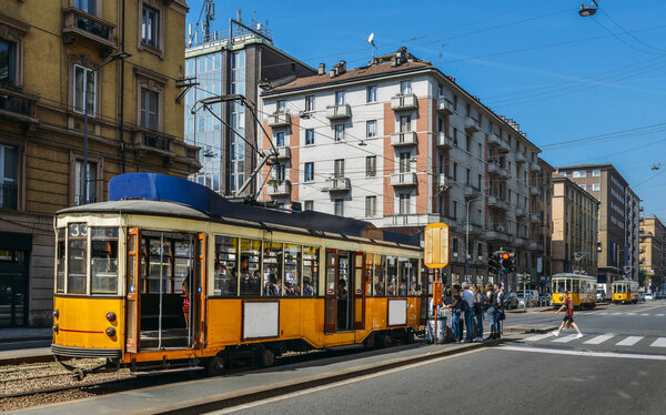 Passengers boarding a traditional yellow tramsway in a busy city centre