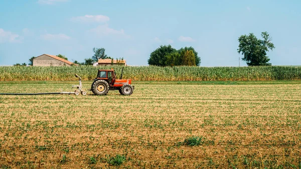 Tracteur rouge portant un tuyau d'eau dans le champ par une belle journée ensoleillée bleue — Photo