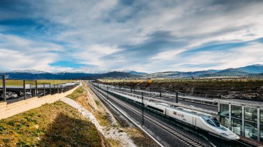 Yüksek hızlı Ave Renfe treni arka planda karlı dağlarla Segovia tren istasyonuna yanaşıyor.
