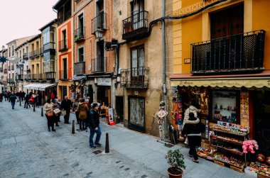 İspanya 'nın tarihi merkezi Segovia' daki hediyelik eşya dükkanlarıyla dolu bir cadde boyunca yürüyen turistler