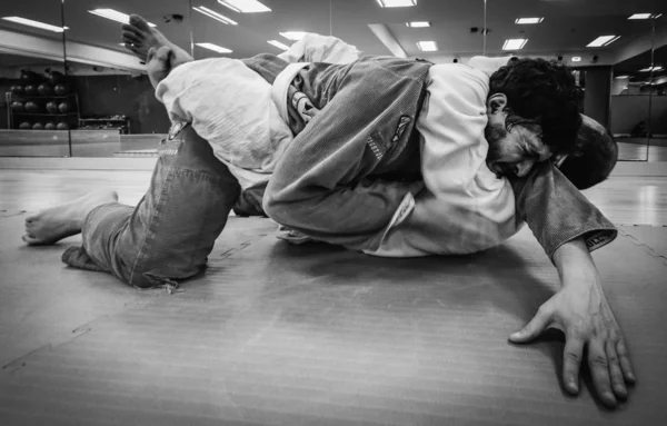 Two young men practice Brazilian Jiu-Jitsu sparring, a grappling type martial arts with a kimono gi - NOT STAGED CONTENT OR AT CLOSED EVENT — Stock Photo, Image