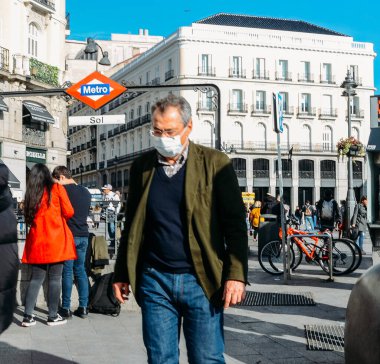 Madrid, İspanya - 7 Mart 2020: Yaşlı adam Madrid, İspanya 'da Puerta del Sol' da kalabalık halinde yürüyen Coronavirus 'a karşı cerrahi maske takıyor