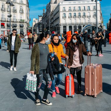 Madrid, Spain - March 7, 2020: Recently arrived Asian tourists with luggage wear surgical mask face protection against Coronavirus walking in crowds at Puerta del Sol in Madrid, Spain clipart