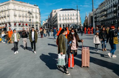 Madrid, İspanya - 7 Mart 2020: Kısa bir süre önce gelen bagaj maskeli Asyalı turistler, İspanya 'nın Madrid kentindeki Puerta del Sol kentindeki kalabalıklar arasında yürüyen Coronavirus' a karşı koruma altına alındı