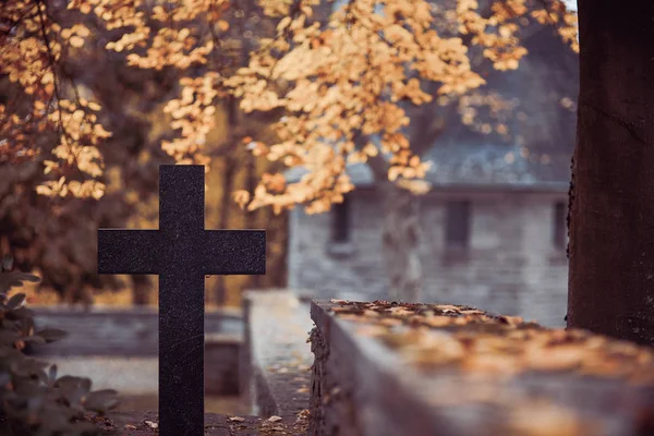 Cross black stone in autumn in front of a mausoleum at the cemetery wall