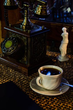 Retro telefon ve kahve masasında sıcak bir içecek olan beyaz bardak..