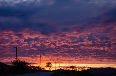 Kırmızı, kıpkırmızı günbatımı bir elektrik hattının dış hattının arka planında.