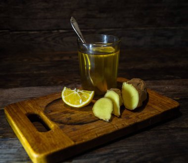  Bardakta limonlu çay, zencefil kökü ve mutfak tahtasında bir dilim limon..