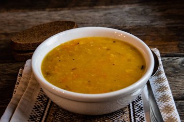 Mutfak peçetesinin üzerinde beyaz bir seramik kasede bezelye çorbası eski ahşap tahtaların arka planında. Ev yapımı yemekler..