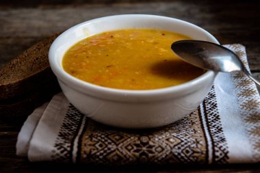 Mutfak peçetesinin üzerinde beyaz bir seramik kasede bezelye çorbası eski ahşap tahtaların arka planında. Ev yapımı yemekler..