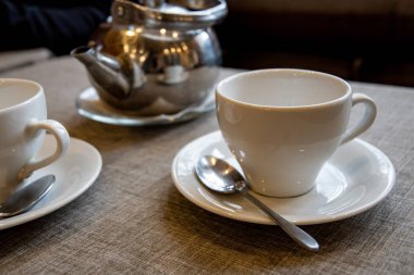 Çay demlemek için metal bir çaydanlık, beyaz bir seramik bardak, kafedeki masada duran şeker için cam bir vazo..