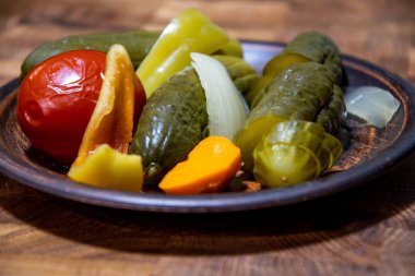Pickled vegetables, cucumbers, tomatoes seasoning on a clay ceramic plate, on a wooden kitchen board.