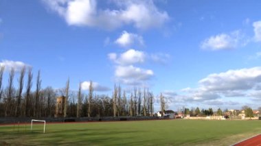 zaman atlamalı küçük standları ve çevresindeki ağaçlar ile bir futbol stadyumu