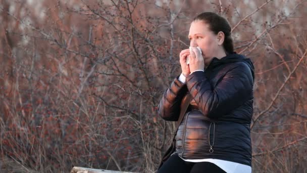 黒の冬のジャケットの中年の女性は公園のベンチでティッシュで鼻をクリアします — ストック動画