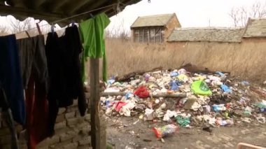 Yıkanmış eski çamaşırlar kabloyla kurumuş ve bir kır evinin bahçesinde bir çöp yığını.