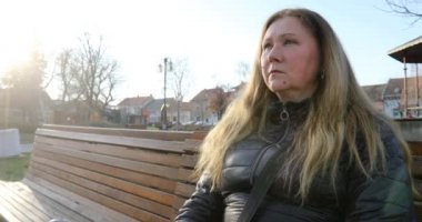 Yüzüne koruyucu maske takan endişeli bir kadının yarım profili. Covid 19. Kadın güneşli bir günde bankta oturuyor..