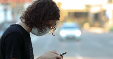 Şehir sokaklarında koruyucu maskeli ve akıllı telefonu olan genç bir adamın profili..