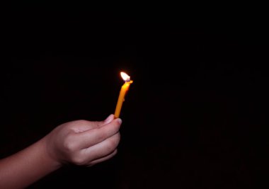 Karanlık bir gecede sönmüş arka planda yanan bir mumu tutan el.